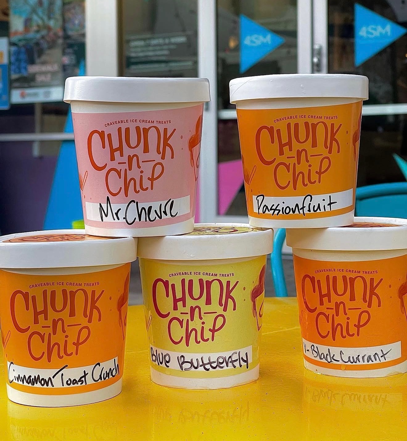 Five Chunk-N-Chip ice cream pints with handwritten flavor labels stacked on a yellow table