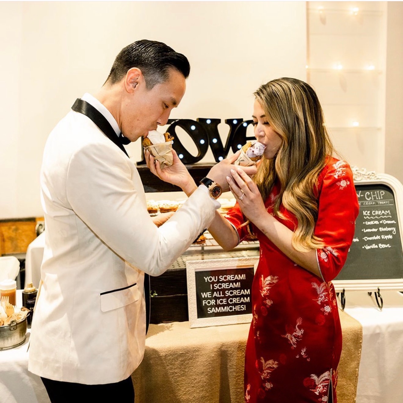 A wedding couple sharing Chunk-N-Chip cookie ice cream sandwiches beside their dessert station